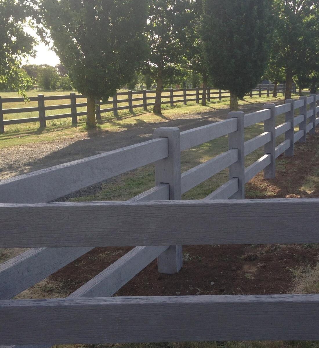 Timber-look concrete post and rail fence running between trees