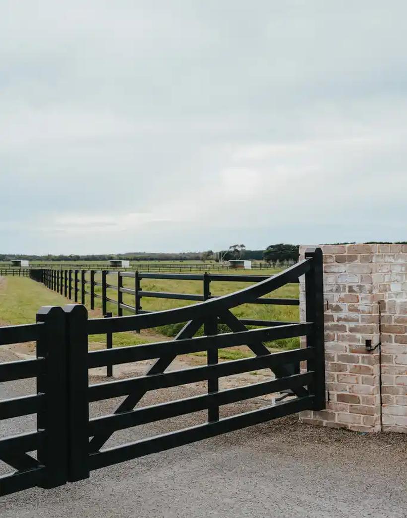 Black timber entry gate hung against a brick pier with the fence line running away behind it