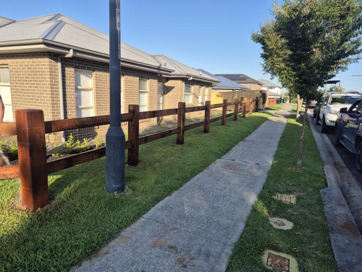 Two rail hardwood fence running along a residential footpath