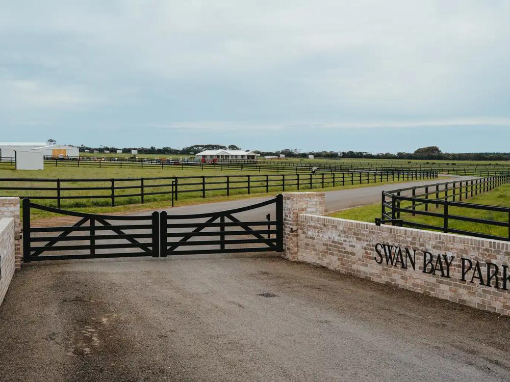 Black entry gates hung between brick piers with post and rail running either side