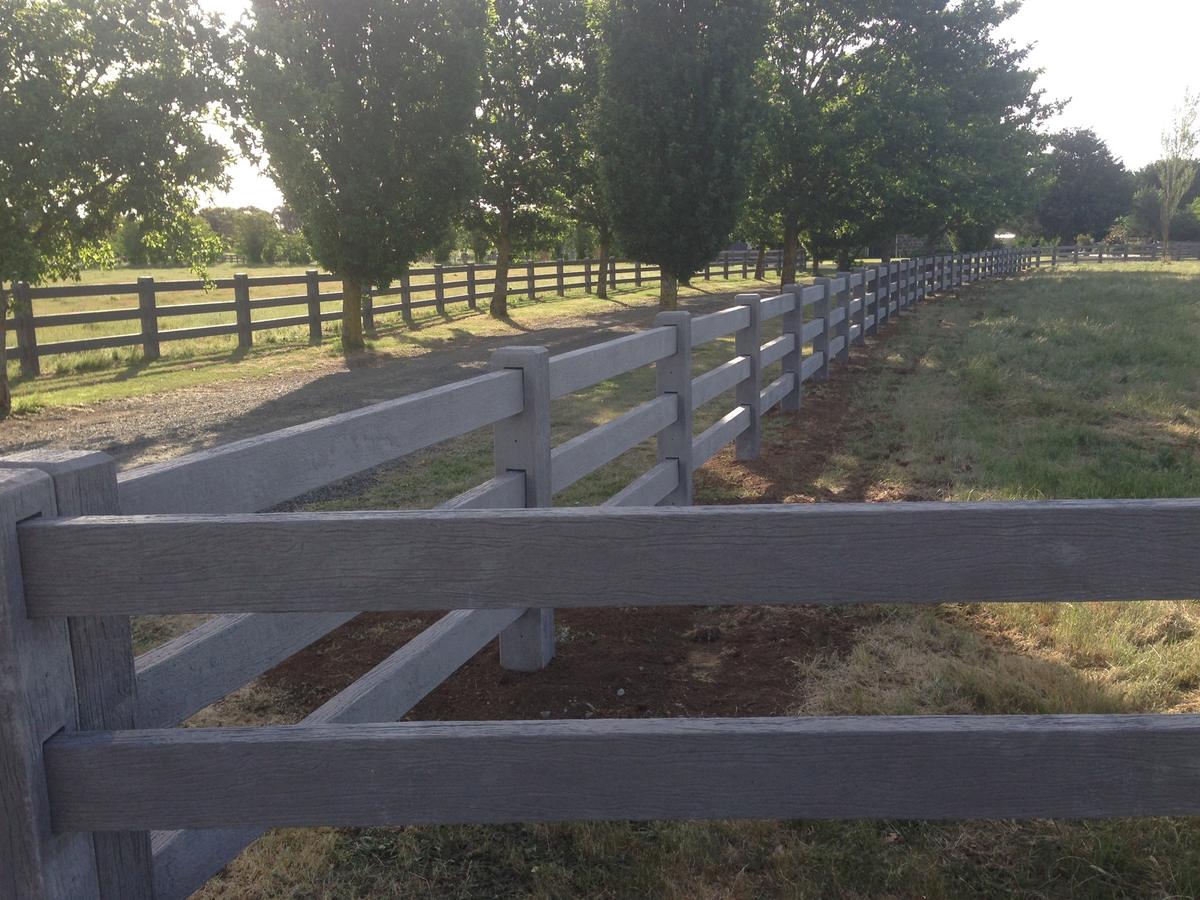 Timber-look concrete post and rail fence between an avenue of trees