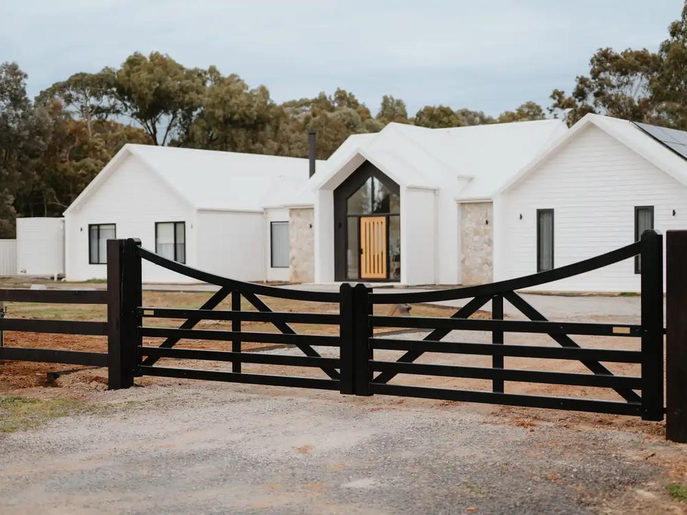 Black timber entry gates in front of a white homestead